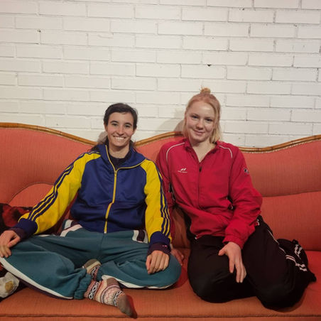 Två personer sitter i en rosa soffa med vit vägg bakom.