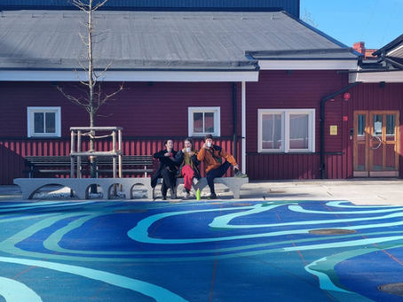 3 personer sitter i vårsolen och dricker kaffe på en bänk utanför Stenkrossens kulturhus