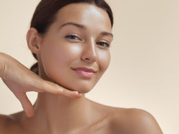 A woman with a glowing complexion gently supports her chin with her hand, exuding confidence and natural beauty against a soft, neutral background.