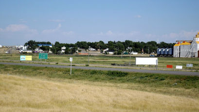 Rural town landscape with fields, road signs, and grain silos. Green trees and buildings are visible 