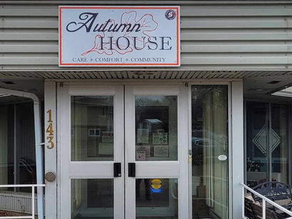 Entrance of a building labeled "Autumn House" with a sign reading "Care * Comfort * Community." Glass doors, beige siding, address 143.
