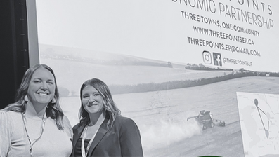 Two people smiling in front of a screen displaying "Three Points Economic Partnership" info. Background shows a rural landscape.