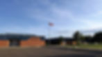 Gull Lake School exterior with Canadian flag on a pole. Blue sky, brick building, and green lawn create a peaceful, sunny scene.