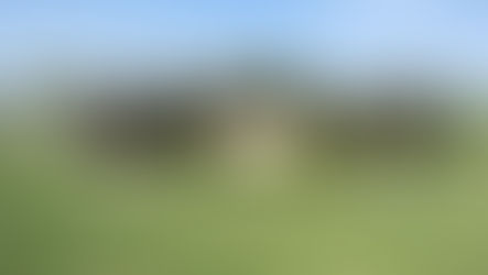 Sign reading "Welcome to Gull Lake" surrounded by greenery and a small black oil pumpjack on a sunny day.