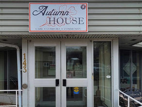 Autumn House entrance with sign reading CARE COMFORT COMMUNITY, number 143, and glass double doors under a gray awning.