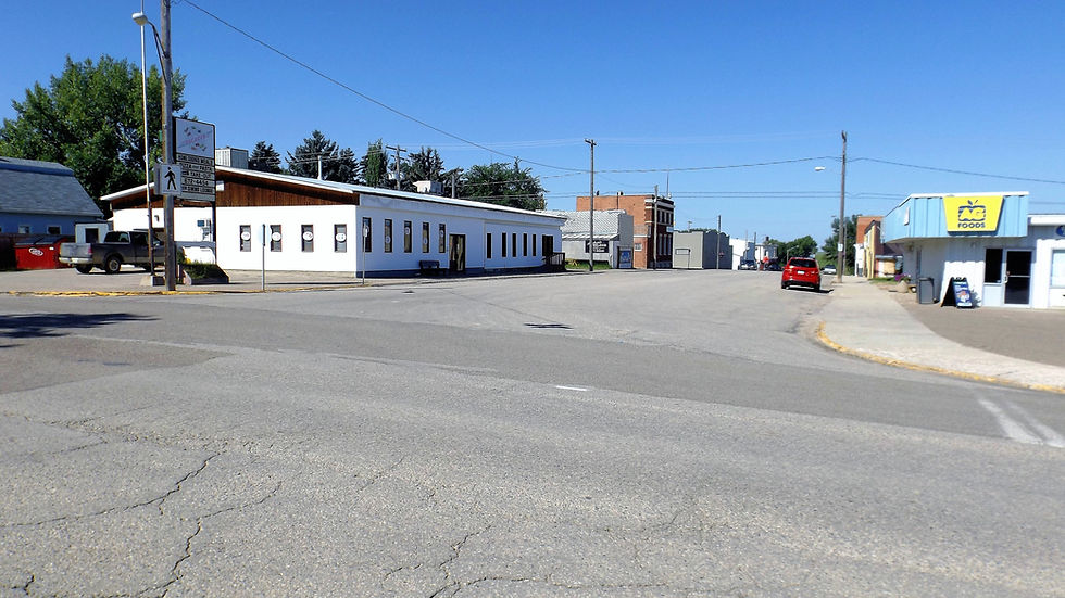 Quiet Gull Lake Main Street with a white building, AG Foods shop, and a parked red car. A clear blue sky adds to the calm atmosphere.