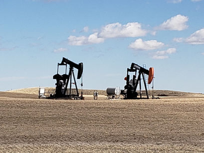 Two oil pumpjacks in a barren field under a blue sky with scattered clouds.