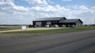 Gray building with parked cars in front, set in a vast rural landscape under a partly cloudy sky. A sign reads "JK Environmental."