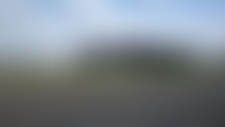 Gray building with parked cars in front, set in a vast rural landscape under a partly cloudy sky. A sign reads "JK Environmental."