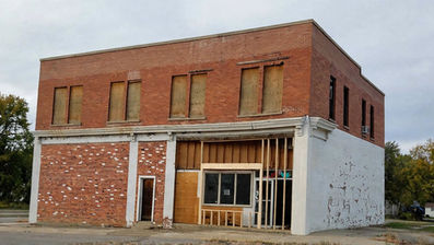 Boarded-up abandoned two-story brick building with peeling white paint and cloudy sky in a quiet street.