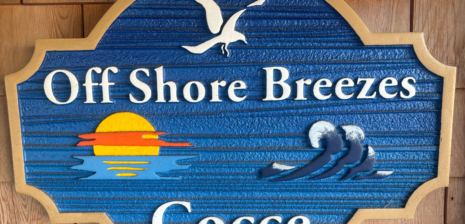 Off Shore Breezes Cocce sign mounted on wooden wall.