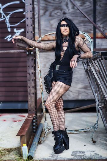 Kayla Bee posing in a metal scrap yard, dressed in all black.