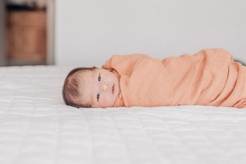 swaddled baby lying on her side on a bed