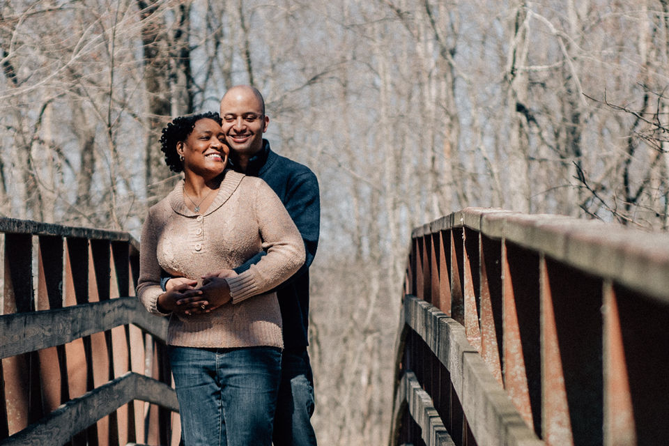 couple smiles and hugs on a bridge