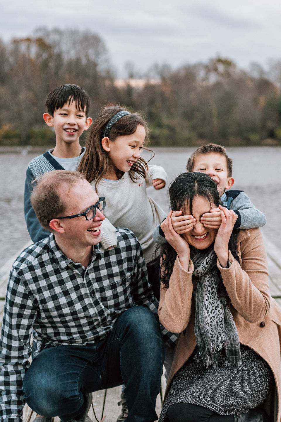 family of five smile and laugh playfully on dock by lake
