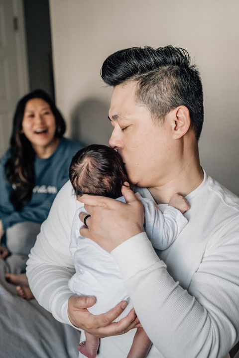 dad kisses baby while mom smiles in the background