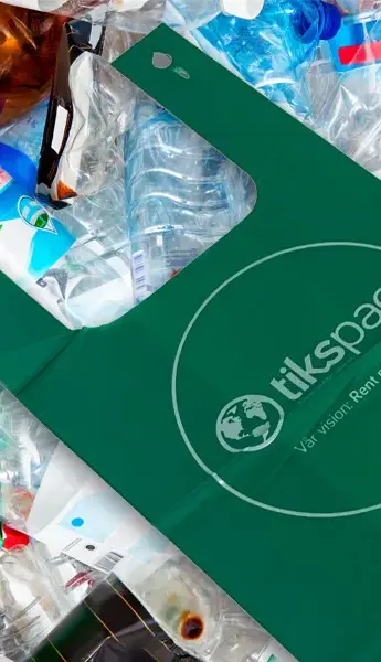 Närbild på grön TiksPac skräppåse i återvunnet PCR-material bland plastflaskor och förpackningar. Påsen är en del av TiksPacs hållbara koncept för en renare miljö.