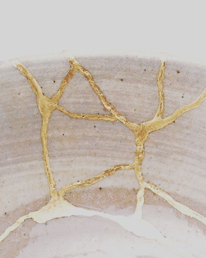 Dettaglio di una ciotola in ceramica riparata con la tecnica giapponese kintsugi, con crepe ricostruite mediante linee irregolari di lacca dorata su superficie chiara.