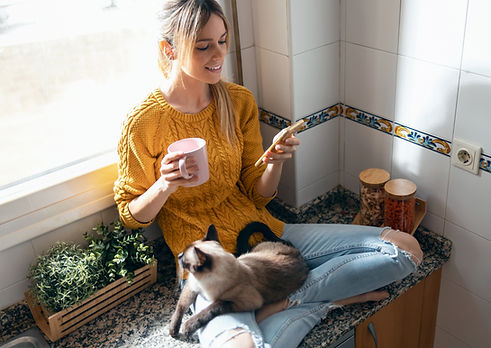 Shot of pretty young woman with her cute cat using mobile phone while drinking coffee sitt