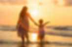 Mother and daughter holding hands at the shoreline, walking into the ocean during a golden sunset, symbolizing connection and peace