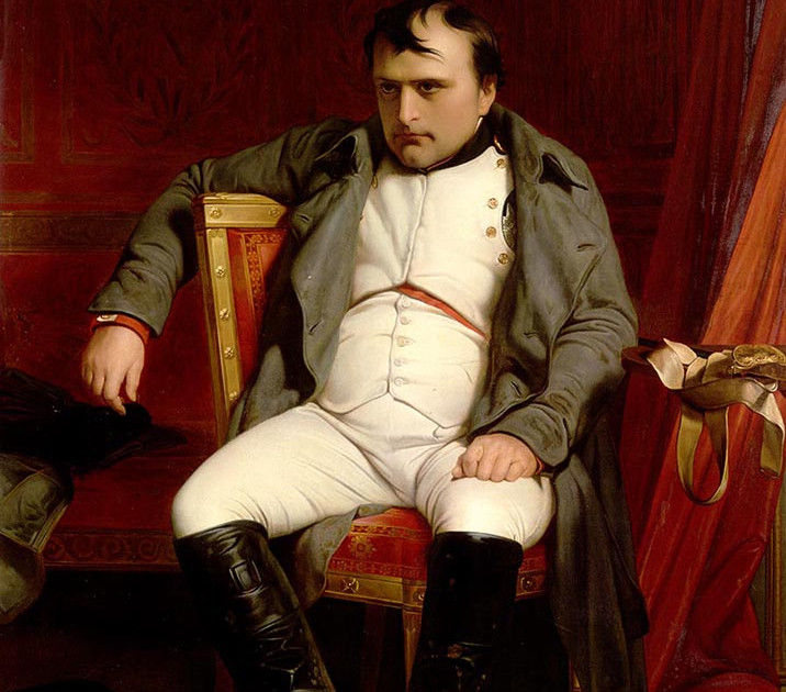 Napoleon Bonaparte sits sternly in a chair, wearing a white uniform, gray coat and black boots, against a deep red backdrop.