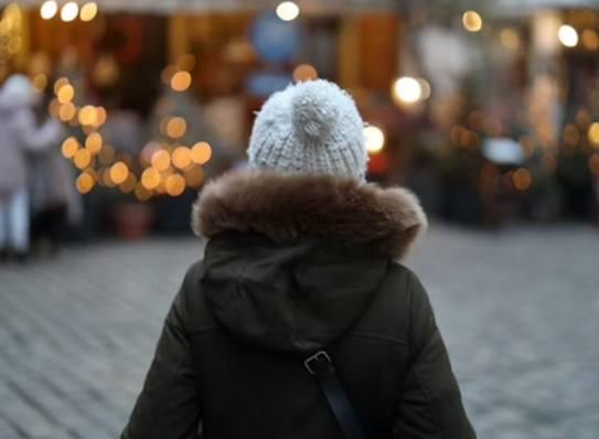 Woman seen from back with winter hat and coat on looking at holiday lights on storefront