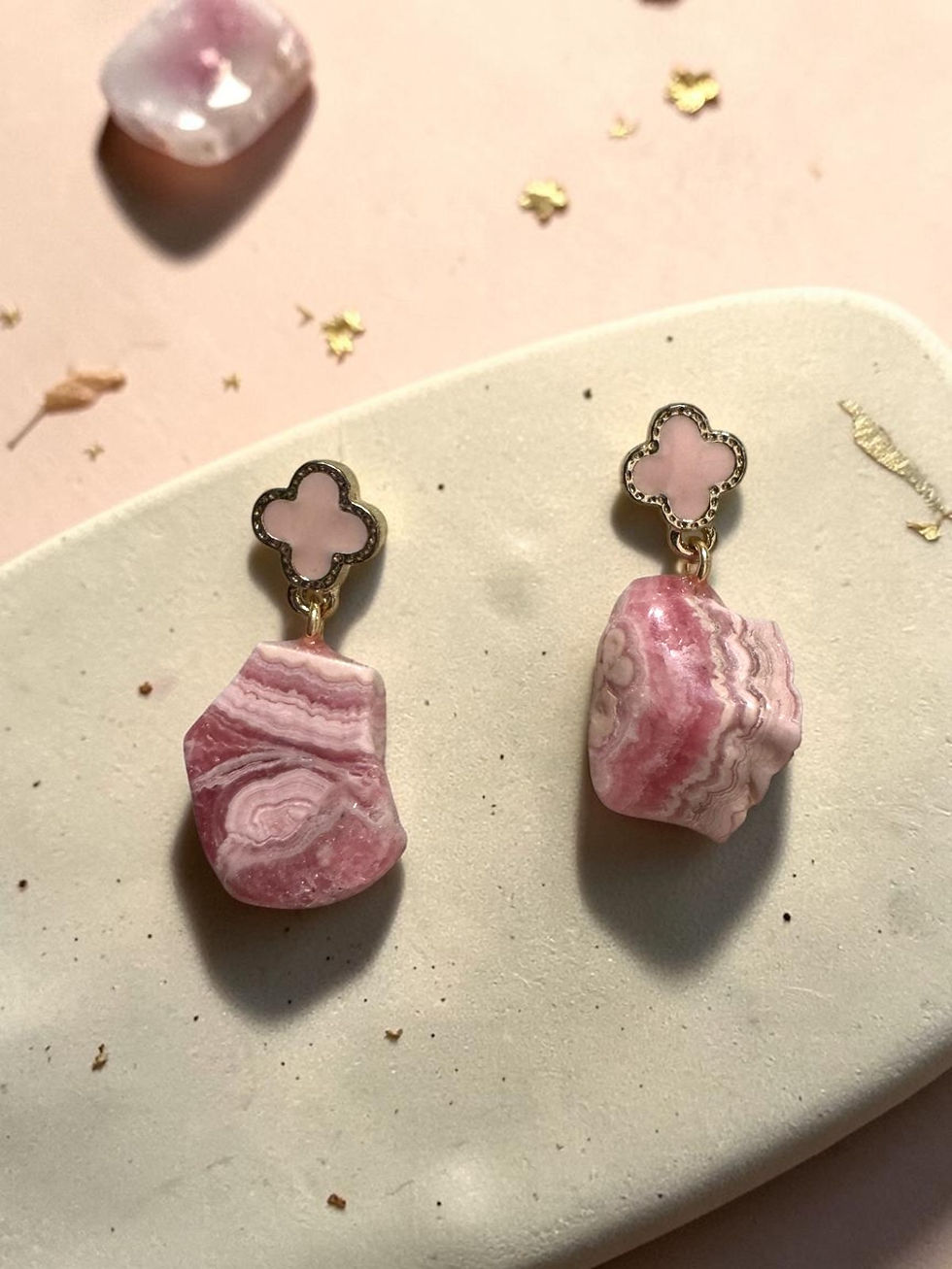 Brincos artesanais Calma Rosada da Tula, com pedra natural de rodonita em tons de rosa e detalhe dourado em trevo.