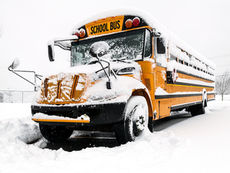 Yellow school bus covered in snow during winter storm conditions in Canada.