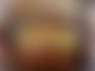 Burger with lettuce, tomato, and onion in an open fast-food box. Gloved hands hold the box. Brown box lid has diagonal stripes.