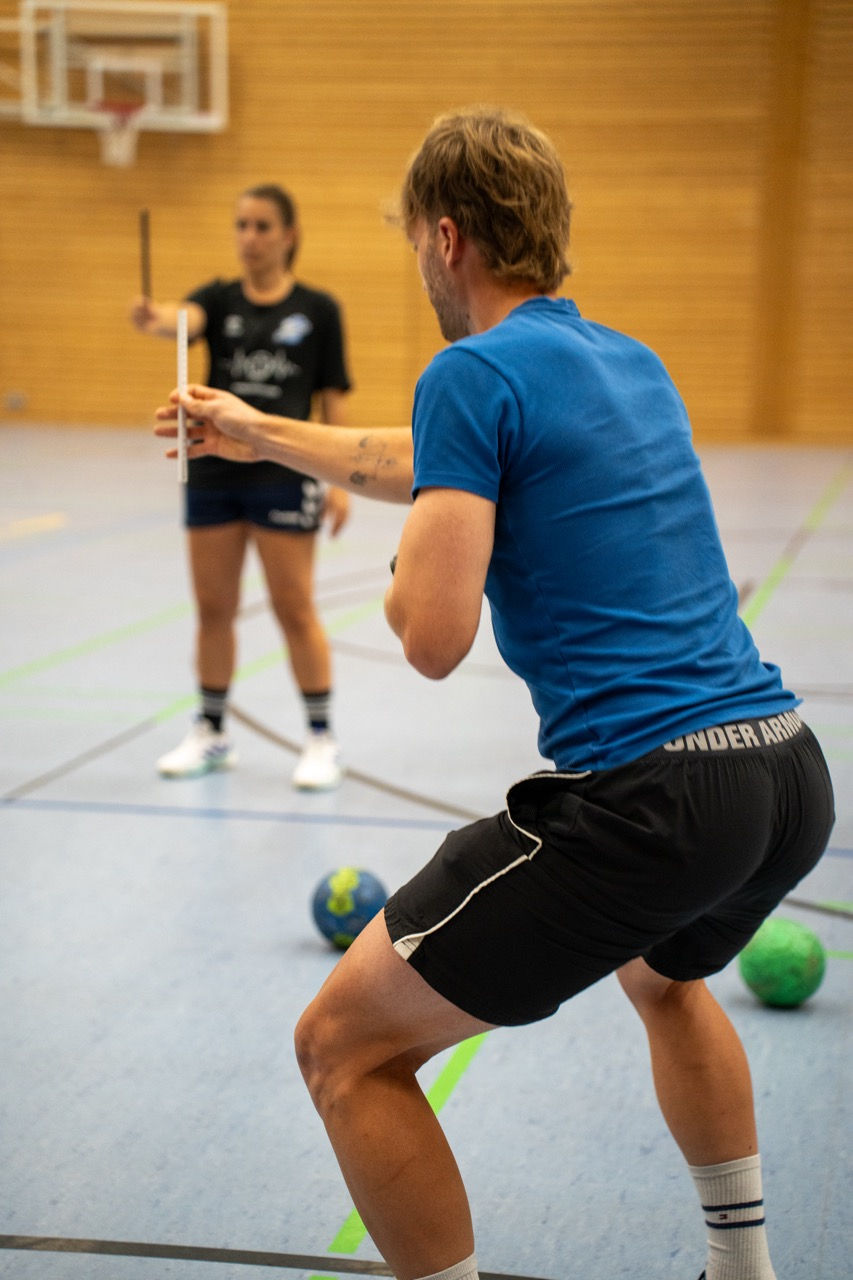 Patrick Keicher misst mit einem Lineal in einer Sporthalle, im Hintergrund steht eine Sportlerin.