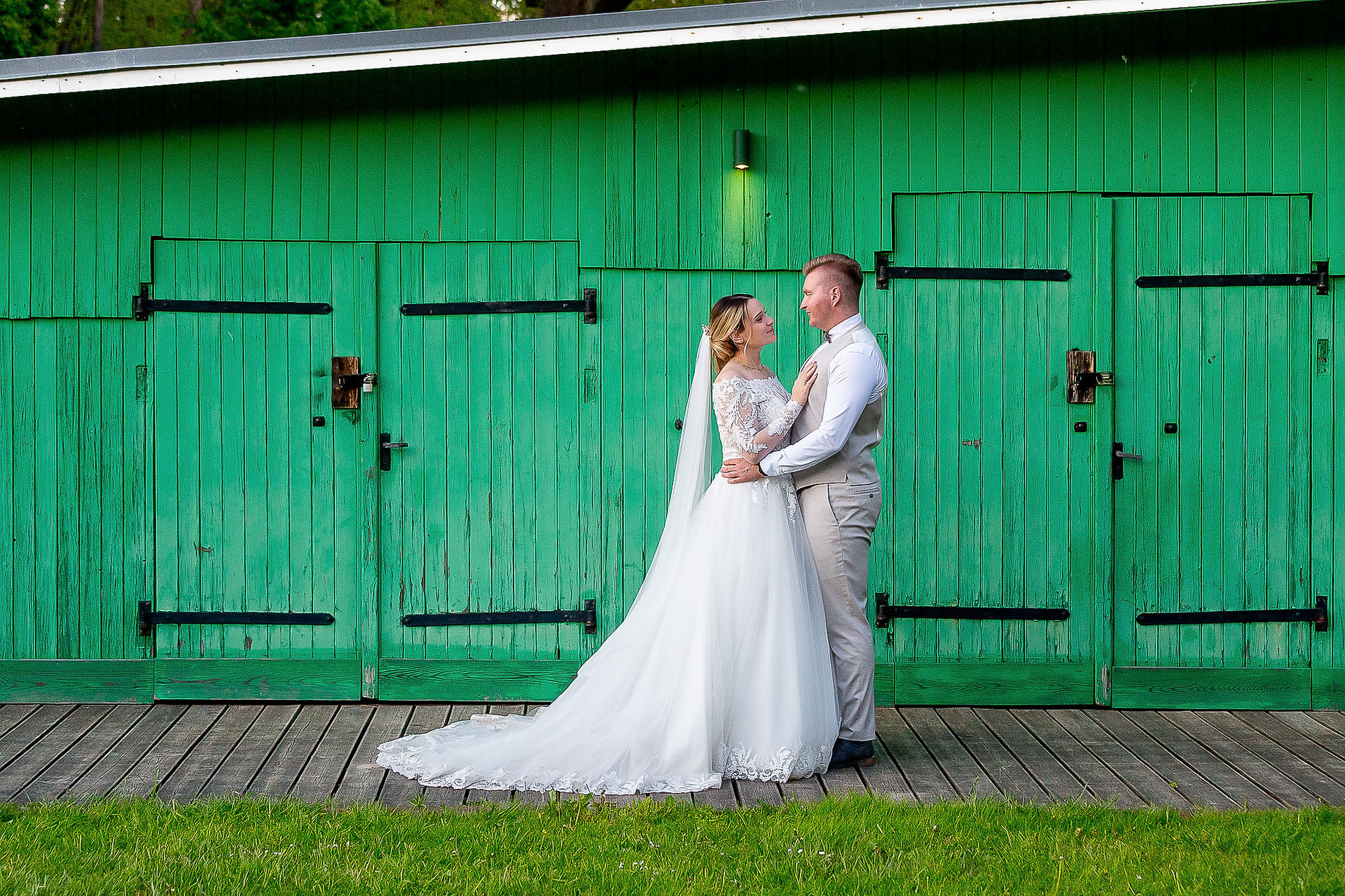 Hochzeitspaar steht sich gegenüber, und im Hintergrund ist ein grünes Holz-Bootshaus an der Hochzeitlocation Lavenda am See zu sehen.