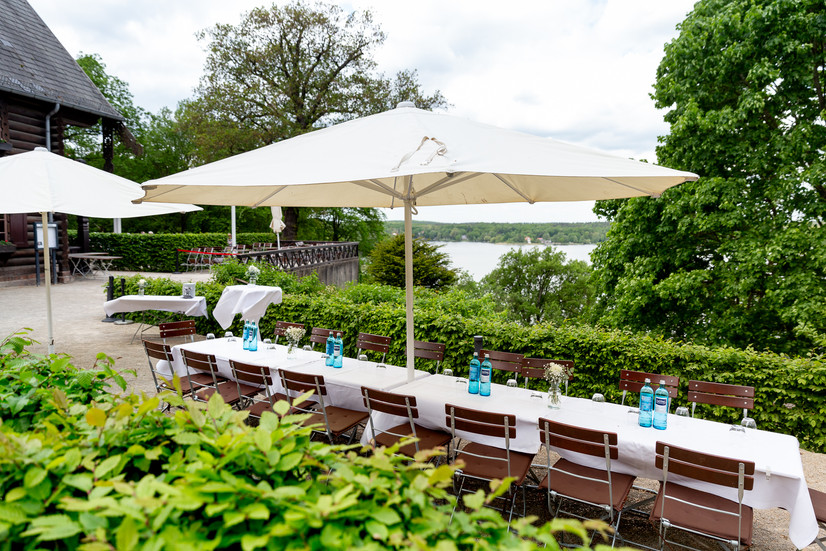 Außenterrasse mit weißen Sonnenschirmen und Blick ins Grüne im Blockhaus Nikolskoe Berlin Wannsee