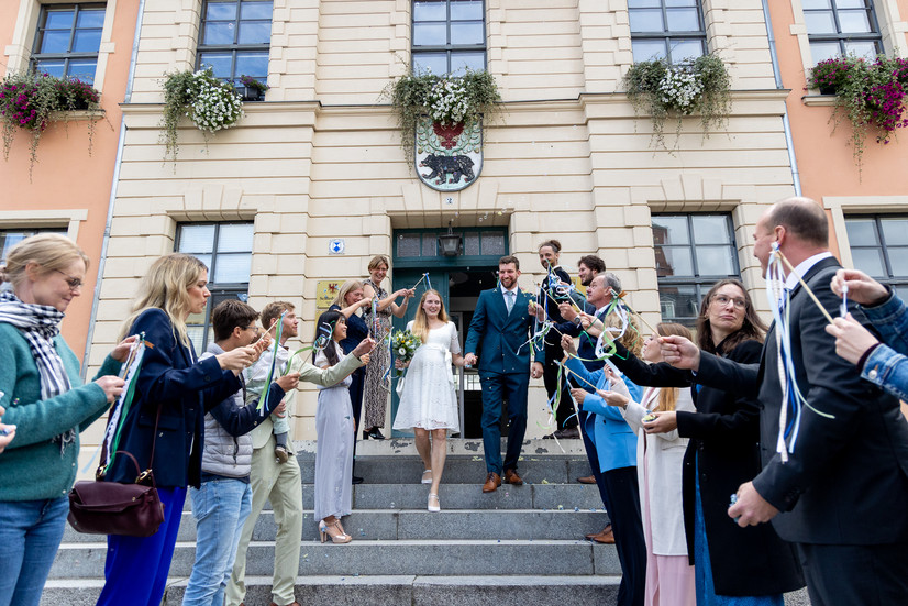 Die Gäste haben sich auf den Stufen des Bernau-Gebäudes versammelt und applaudieren dem Brautpaar, als dieses die Stufen hinuntersteigt und die Gäste anblickt. Alle sind glücklich!