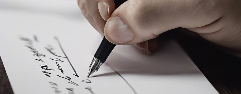 Eine Nahaufnahme einer Hand, die einen Stift hält und eine Unterschrift auf ein weißes Blatt Papier schreibt.