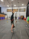 People perform aerial bungee fitness handstands in a gym with black mats.  