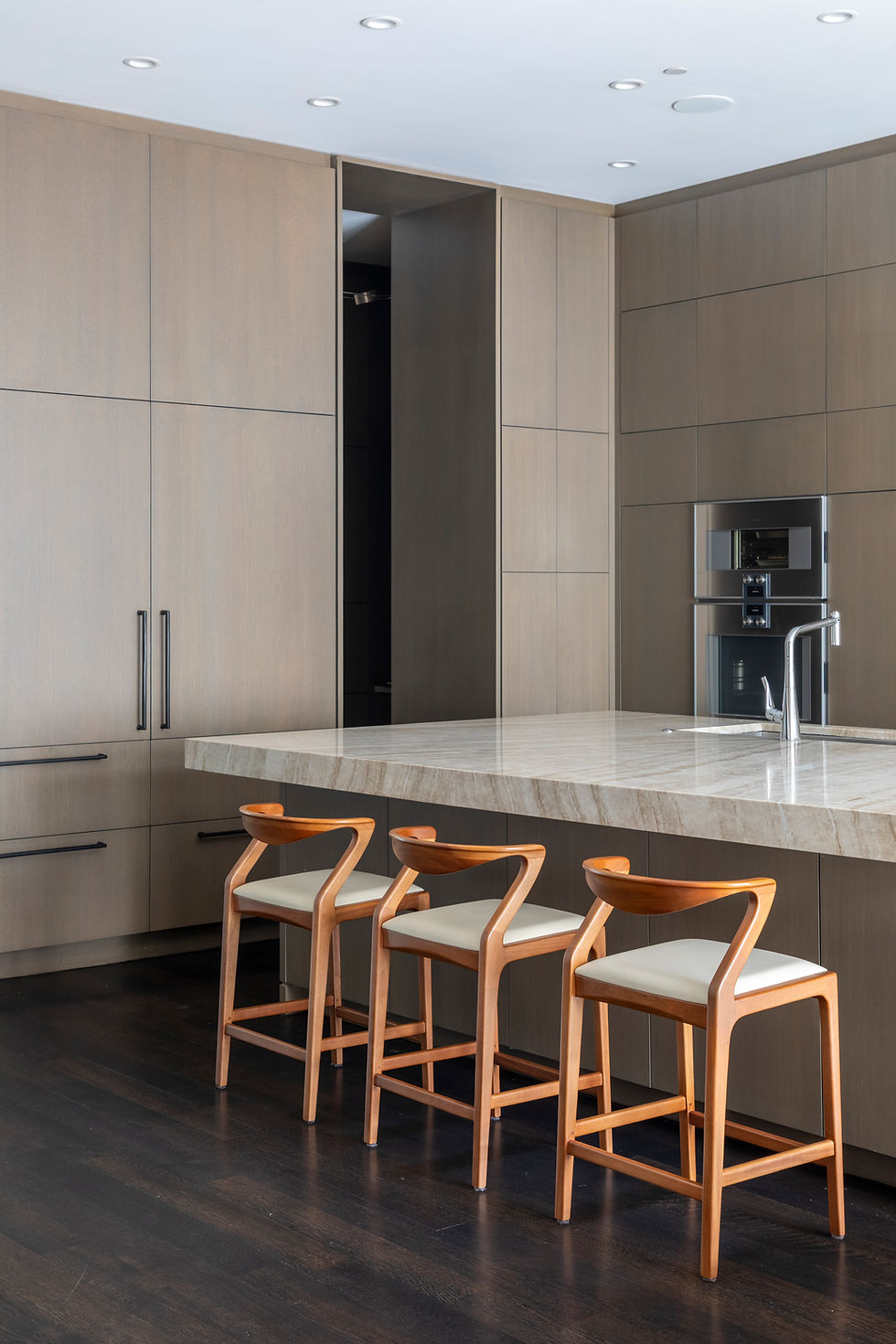 Contemporary kitchen with integrated wood cabinetry and Duda stools by Aristeu Pires, emphasizing proportion, materiality, and the balance between structure and warmth.