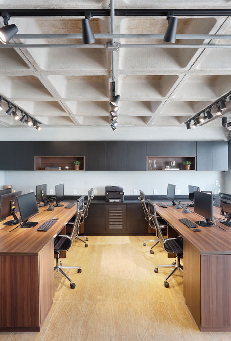 Commercial office design in Rio de Janeiro with custom wood workstations, ergonomic task chairs, track lighting, and exposed concrete ceiling