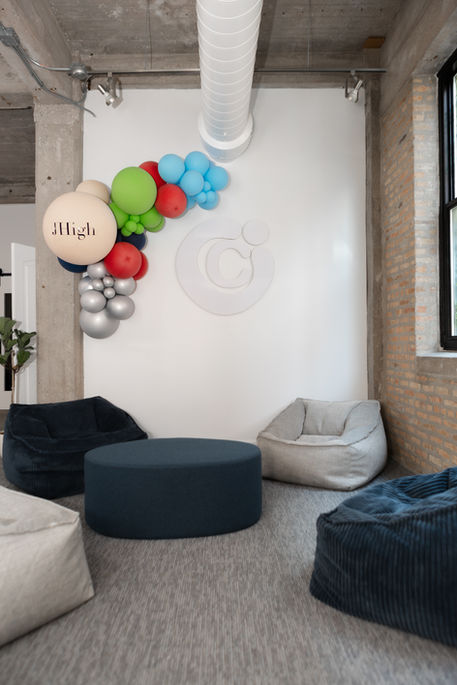 High school lounge area at City Church Chicago with soft seating, poufs, exposed concrete details, and a colorful balloon installation on a white feature wall.