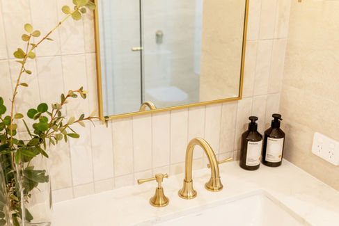Close-up of bathroom vanity in Nedlands Perth featuring brushed gold tapware, stone benchtop, decorative styling and wall-mounted mirror – luxury renovation by Elite Makeovers.