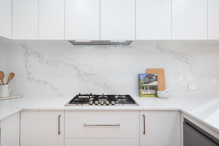 Close-up of marble-look splashback and gas cooktop with upper white cabinetry – Attadale, Perth
