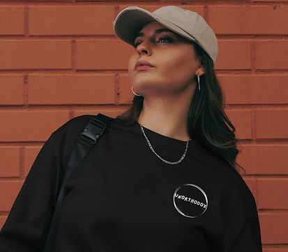 A WOMAN WEARING AN UNORTHDOX LOGO SWEATER STANDING IN FRONT OF A BRICK WALL