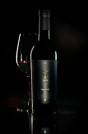 Dunkle Weinflasche mit Weinglas vor schwarzem Hintergrund in edler Lichtstimmung