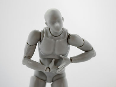 Gray plastic figurine holding its abdomen, suggesting tension or discomfort