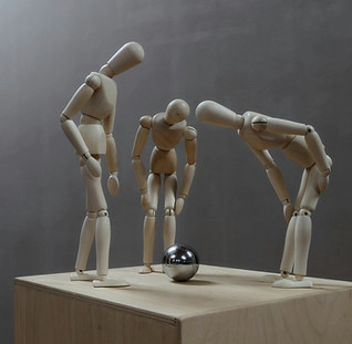 Three wooden artist mannequins leaning down to observe an object on the floor