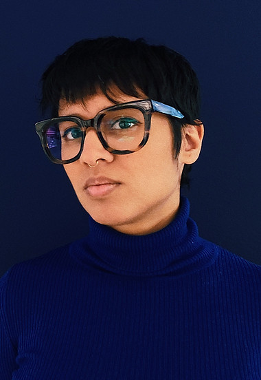 Tanya wearing glasses and a blue turtleneck in front of a blue background.