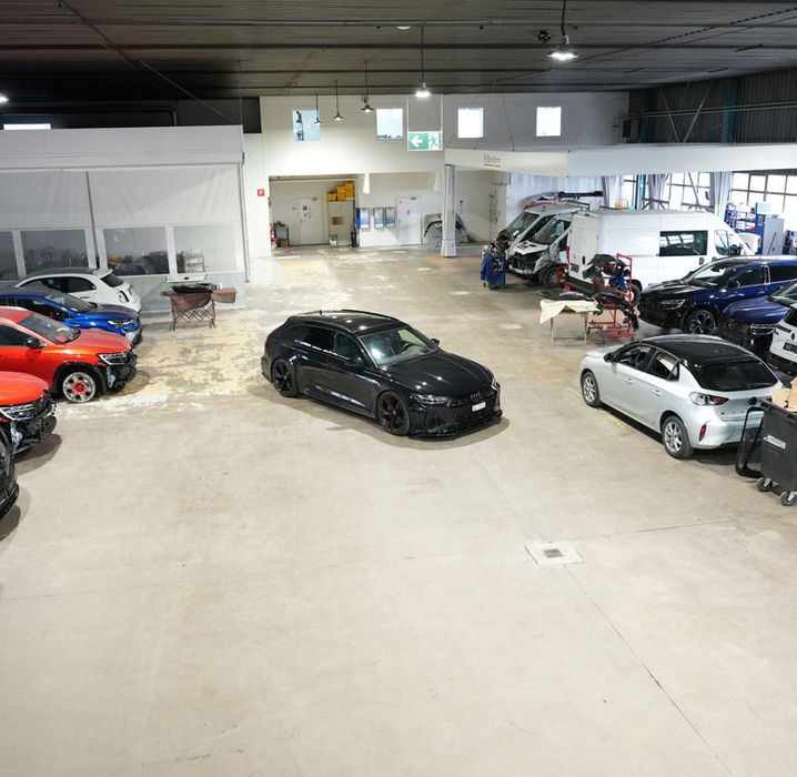 Atelier de réparation automobile spacieux avec plusieurs voitures garées en attente.