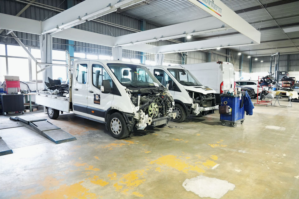 Deux fourgons blancs démontés dans un grand atelier de réparation automobile.