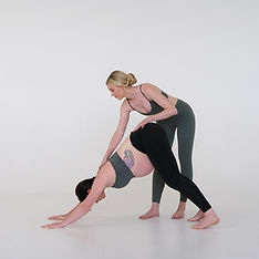 Instructor assisting woman in downward dog yoga pose.