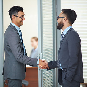 The image shows three businessmen in an office setting, with two of them shaking hands, possibly finalizing a deal or agreement. The context from the search results indicates that the image is related to "Partnership Liquidation: Guide to Retirement and Dissolution", suggesting the handshake could represent the conclusion of a partnership or a business transaction. The third businessman stands to the side, seemingly observing the interaction. The office environment, with blinds and glass partitions, indicates a professional setting. The overall impression is one of business dealings and formal agreements. 
