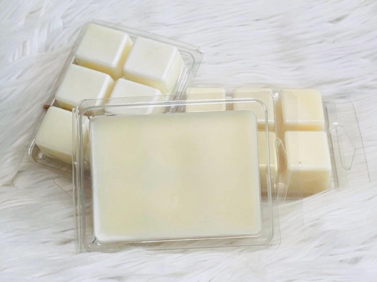 White wax melts in clear plastic containers on a fluffy white surface.